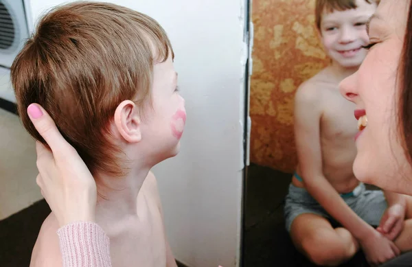 Mom kisses her son on the cheek and leaves a trace of lipstick. Theyre sitting in front of the mirror. — Stock Photo, Image