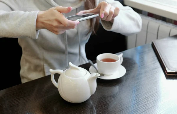 Неузнаваемые женщины держат в руках фотографии чайника и чашки в кафе на телефоне. Вид сбоку . — стоковое фото