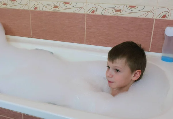 Boy 6-7 years lying in the bath with white foam. — Stock Photo, Image