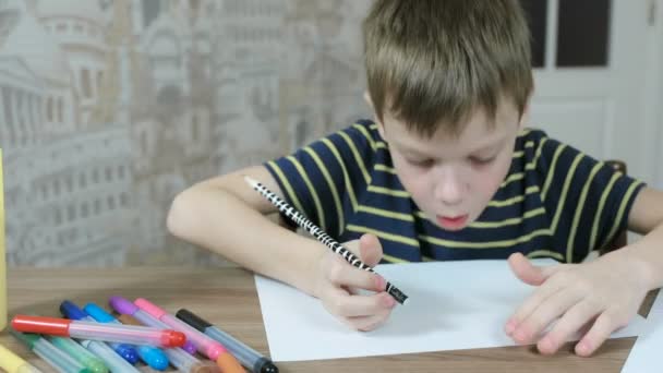 Αγόρι 7 ετών σε ένα ριγέ μπλουζάκι διαγράφει γραμμές από λευκό χαρτί και φυσά μακριά βρωμιά με φύλλο. — Αρχείο Βίντεο