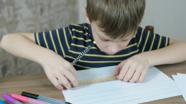 Мальчик 7 лет в полосатой футболке рисует ровные линии на бумаге карандашом и линейкой. Крупный план . — стоковое видео