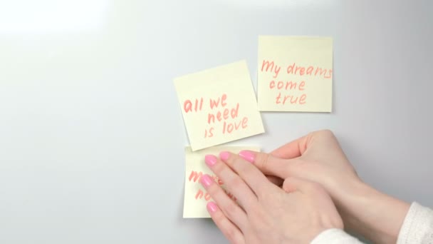 Gros plan womans mains bâton jaune autocollant feuilles de papier avec des phrases de motivation sur un tableau blanc . — Video