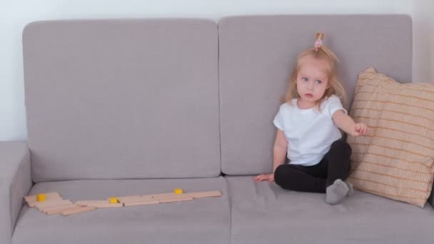 Little charming girl sitting on the sofa talking and playing wood blocks. — Stock Video