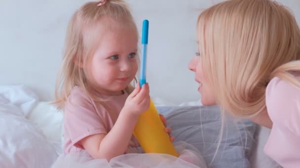 Jovem mulher loira atraente beijar sua pequena filha encantadora em vestidos rosa com canetas de feltro — Vídeo de Stock