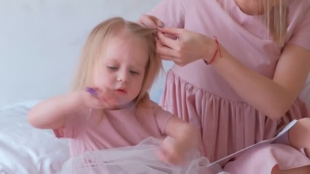 Maman tresse des cheveux à sa petite fille charmante en robes roses pendant qu'elle peint avec feutre-stylo . — Video
