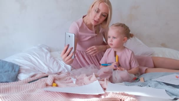 Genç çekici sarışın anne küçük sevimli kızı pembe elbiseler ile hareket eden telefon içinde bir fotoğraf çekmek. — Stok video