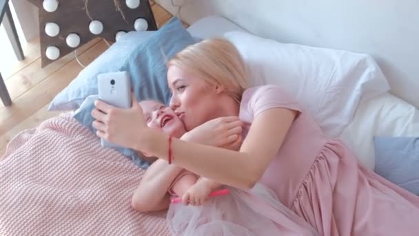 Młody atrakcyjny blond mama zrobić zdjęcie w telefonie komórkowym z córką uroczy mały w różowe sukienki. Rodzina uścisk i pocałunek. — Wideo stockowe