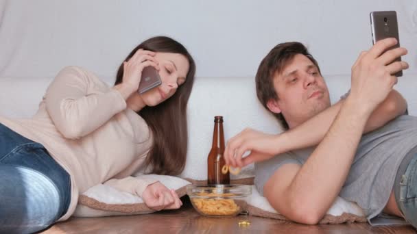 Pár muž a žena jíst chipsy. Žena mluví mobilní telefon, muž procházení svůj mobilní telefon. — Stock video