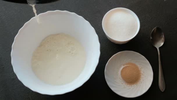 酵母面团的制备。在碗里倒入牛奶, 加入糖和酵母, 拌匀。男性手特写. — 图库视频影像