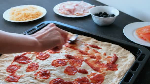 Κοντινό πλάνο γυναικεία χέρια εξαπλώνεται σάλτσα στη ζύμη για πίτσα και επίχρισμα με κουτάλι. — Αρχείο Βίντεο