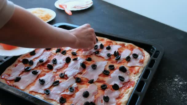 Cook preparing pizza. Closeup womans hands put tomato to dough with sauce and bacon. — Stock Video