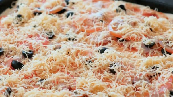 Cook preparing pizza. Closeup pizza with grated cheese, sauce, olives, tomatoes and bacon. — Stock Video