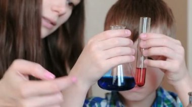 Kimya deneyleri evde. Çocuk bir tüp ve bir şişe farklı renkteki iki sıvı inceliyor.