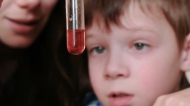 Kimya deneyleri evde. Çocuk annesi ile bir test tüpü içinde kırmızı sıvı inceliyor.