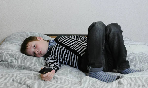 Смотреть телевизор, лежащий на диване. Расстроенный мальчик смотрит телевизор и переключает каналы . — стоковое фото