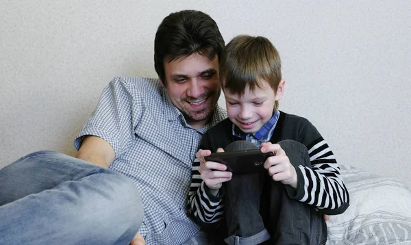 Papá e hijo están viendo algo en el teléfono móvil juntos y sonriendo . — Foto de Stock