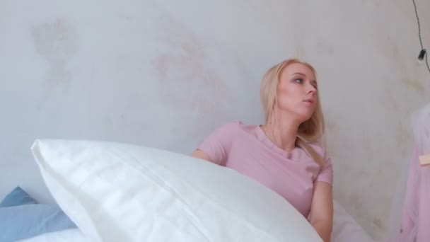 Young attractive blond mom plays with her little charming daughter in pink dresses. Girl falls in pillows. — Stock Video