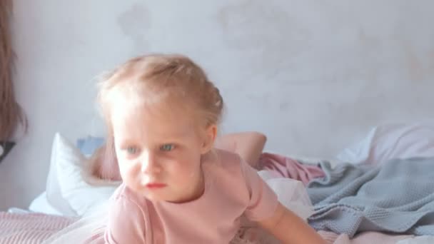 Маленькая очаровательная блондинка играет с баллоном в розовом платье, сидя на кровати . — стоковое видео