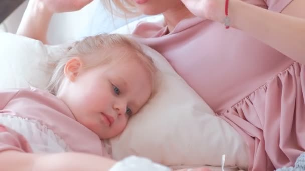 Pequeña chica rubia encantadora juega con el globo con su mamá en vestido rosa acostado en la cama . — Vídeos de Stock