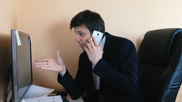 휴대 전화에 컴퓨터에서 하 고 감정적으로 일 하는 젊은 남자 회담. — 비디오