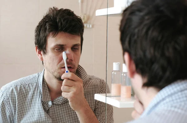 Moe, slaperig man met een kater die heeft net wakker borstel zijn tanden, kijkt naar zijn spiegelbeeld in de spiegel. — Stockfoto