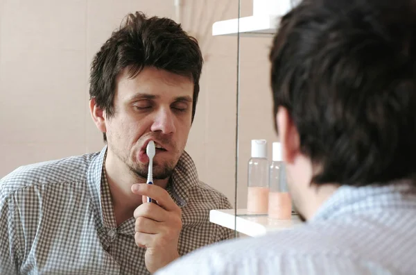 Hombre cansado y somnoliento con resaca que acaba de despertar cepillarse los dientes, mira su reflejo en el espejo . — Foto de Stock