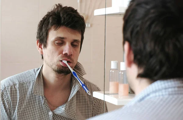 Gemarteld slaperig wakker alleen man voor de spiegel met een tandenborstel in zijn mond. — Stockfoto