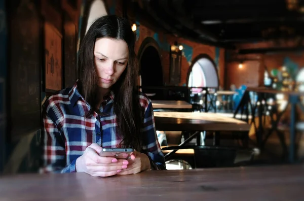 La mujer trastornada envía un mensaje por teléfono sentado en un café. Vestido con una camisa a cuadros . — Foto de Stock