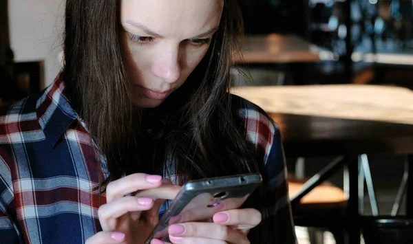 Üzgün bir kadın gönderir, ya da bir kafede oturup telefon Internet kullanın. Bir ekose gömlek giymiş. — Stok fotoğraf