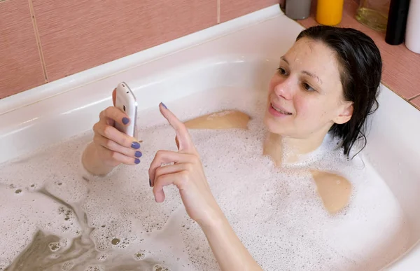 Mujer bruenette charlando en el teléfono móvil durante el baño en casa . — Foto de Stock