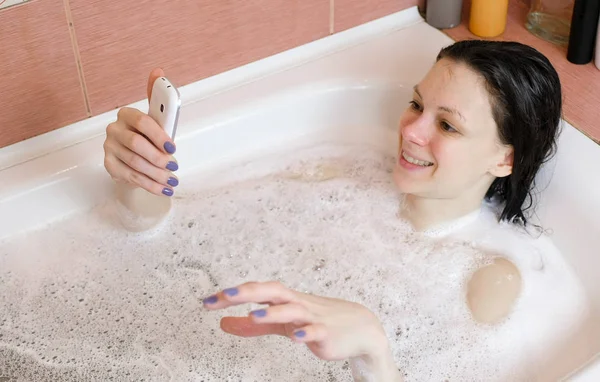 Morena mujer emocional hablando en el chat de vídeo tumbado en el baño. Vista lateral . — Foto de Stock