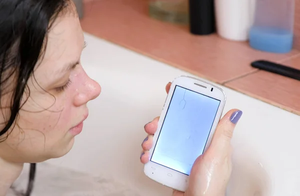 Женщина смотрит на свой мокрый телефон в ванной комнате . — стоковое фото