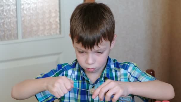 Експерименти з хімії вдома. Хлопчик у картатій сорочці сидить за столом і чистить трубку пензлем. Камера, що рухається донизу . — стокове відео