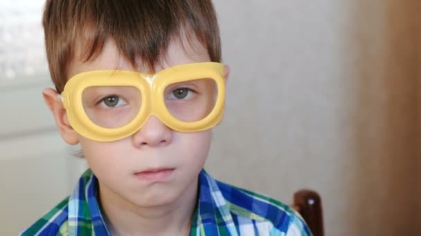 Seriosly boy in safety yellow goggles sitting at the table and looking at camera. Experiments on chemistry at home. — Stock Video