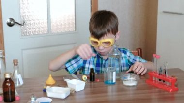 Evde kimya üzerinde deneyler. Çocuk başka bir mavi maddeler ile kabı içine su dökün.