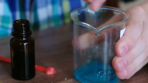 Experimente zur Chemie zu Hause. Nahaufnahme Jungenhände mischen die Substanzen und die blaue Flüssigkeit im Becherglas mit Glasstab. — Stockvideo