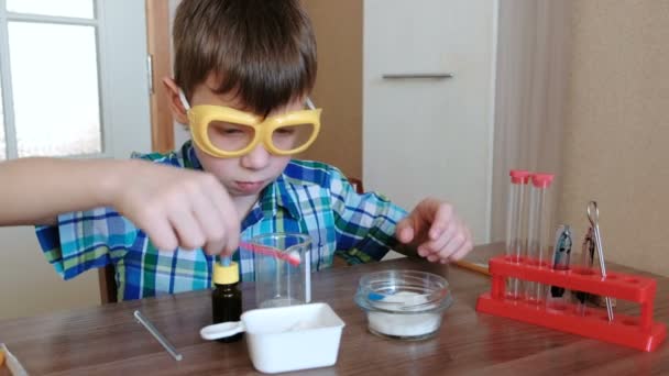 Эксперименты по химии дома. Мальчик смешивает вещества и синюю жидкость в стакане . — стоковое видео