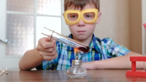 Experimentos de química en casa. Chico calienta el tubo de ensayo con líquido rojo en la lámpara de alcohol ardiente . — Vídeos de Stock