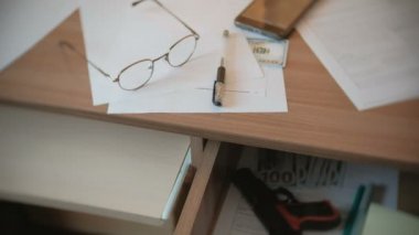 Ahit, kalem, gözlük ve tablo ve silah bir tablo çekmecede para.