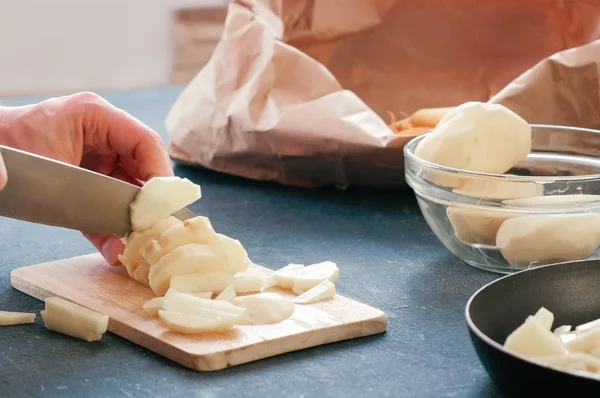 Руки крупным планом режут картошку на деревянной доске и кладут на сковородку с маслом. . — стоковое фото