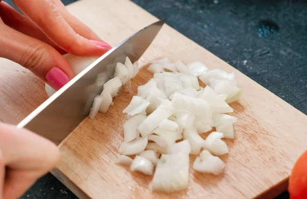 Closeup womans hands cutting an onion on a wood board. — Stock Photo, Image