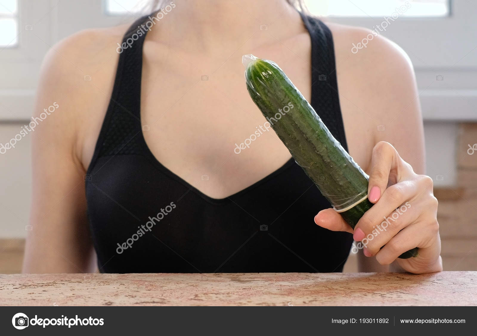 Closeup womans hands with dress the condom on cucumber. Stock.