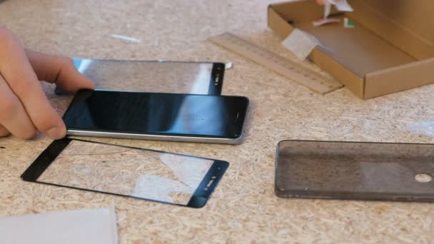 Человек меняет треснувшее защитное стекло мобильного телефона на новое. Вытирает экран телефона тканью. Руки крупным планом . — стоковое видео