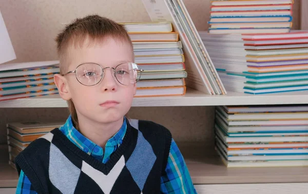 Niño cansado de siete años con gafas sentado en el suelo entre los libros . — Foto de Stock