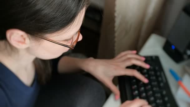 Woman brunette in glasses is typing something on keyboard working on computer. Top view. — Stock Video