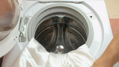 Çamaşırhane. Adam beyaz yatak çarşafları çamaşır makinesine koyar, toz ekler ve içerir.