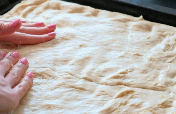 Cooking pizza. Closeup womans hands lays out the dough on a baking sheet, spreading all over the baking sheet pan.