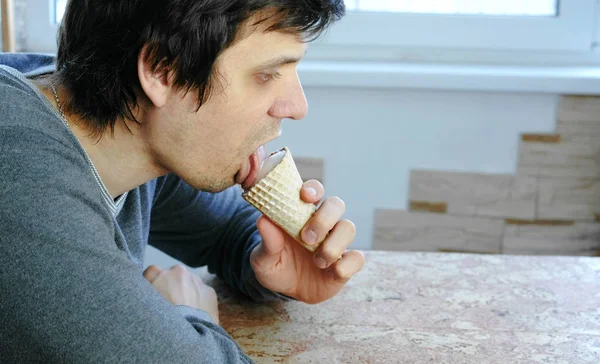 Jonge man eet ijs thuis zitten bij het raam. Zijaanzicht. — Stockfoto