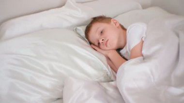 Yedi yaşındaki bir oğlan sessizce onun odasında yatakta döşeme ellerini başının altına koyarak.