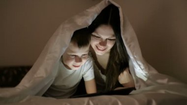 Genç kadın anne ve oğlu birlikte tablet battaniyenin altında bir film izlerken.